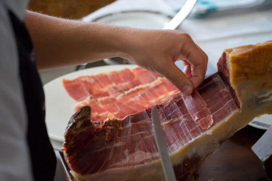 Waiter cutting slices of delicious spanish serrano ham.